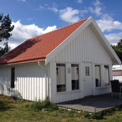 Hytte på Jomfruland camping med hvit trekledning og tak i rødt, idyllisk beliggenhet nær naturen.